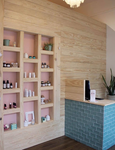 Green City Beauty reception area with wood shelving, skincare products, and teal tiled front desk